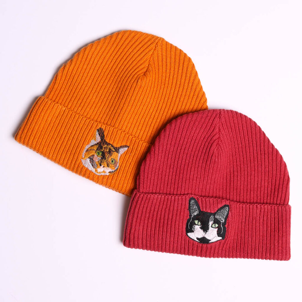 Personalised cat embroidery beanie hats. Orange beanie hat embroidered with a tortoise shell cat and a red beanie hat embroidered with a black and white cat