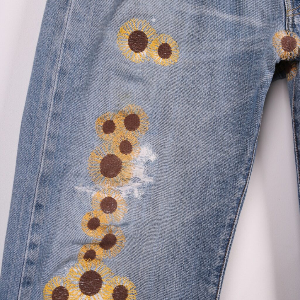 Repaired Levis jeans with sumflower emrboidery. Blue vintage Levi's jeans patch repaired mnay times with yellow and brown emrboidered sunflowers.
