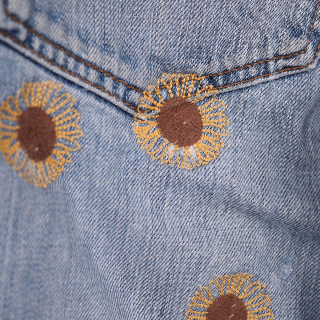 Repaired Levis jeans with sumflower emrboidery. Blue vintage Levi's jeans patch repaired mnay times with yellow and brown emrboidered sunflowers.